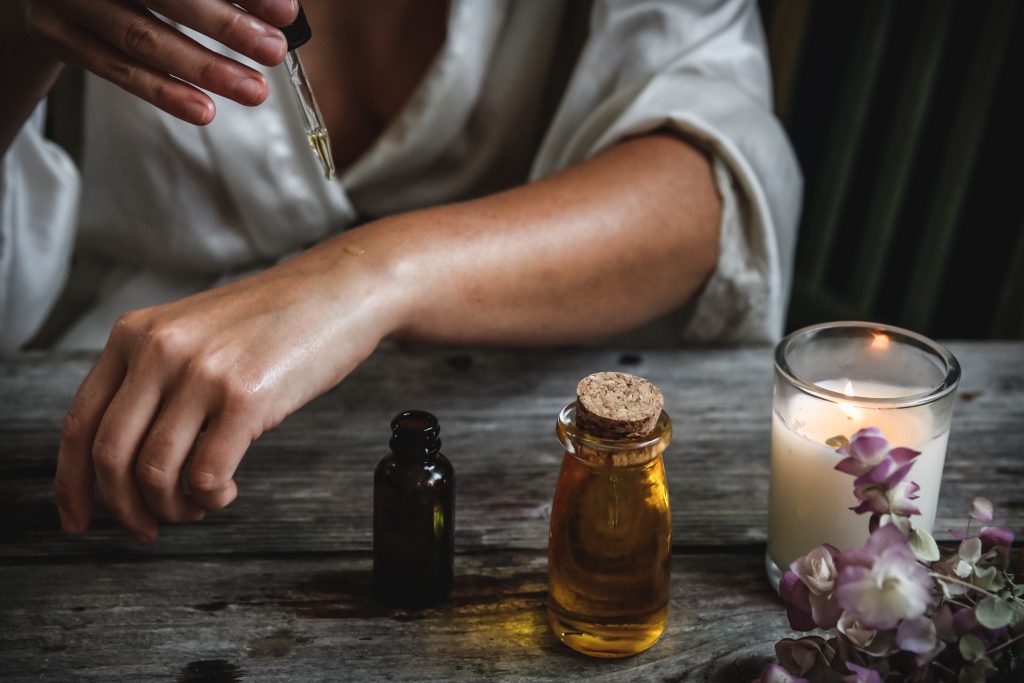 Woman putting rocky montain essential oils on her hand with some oil, a candle and flowers on a table top. 