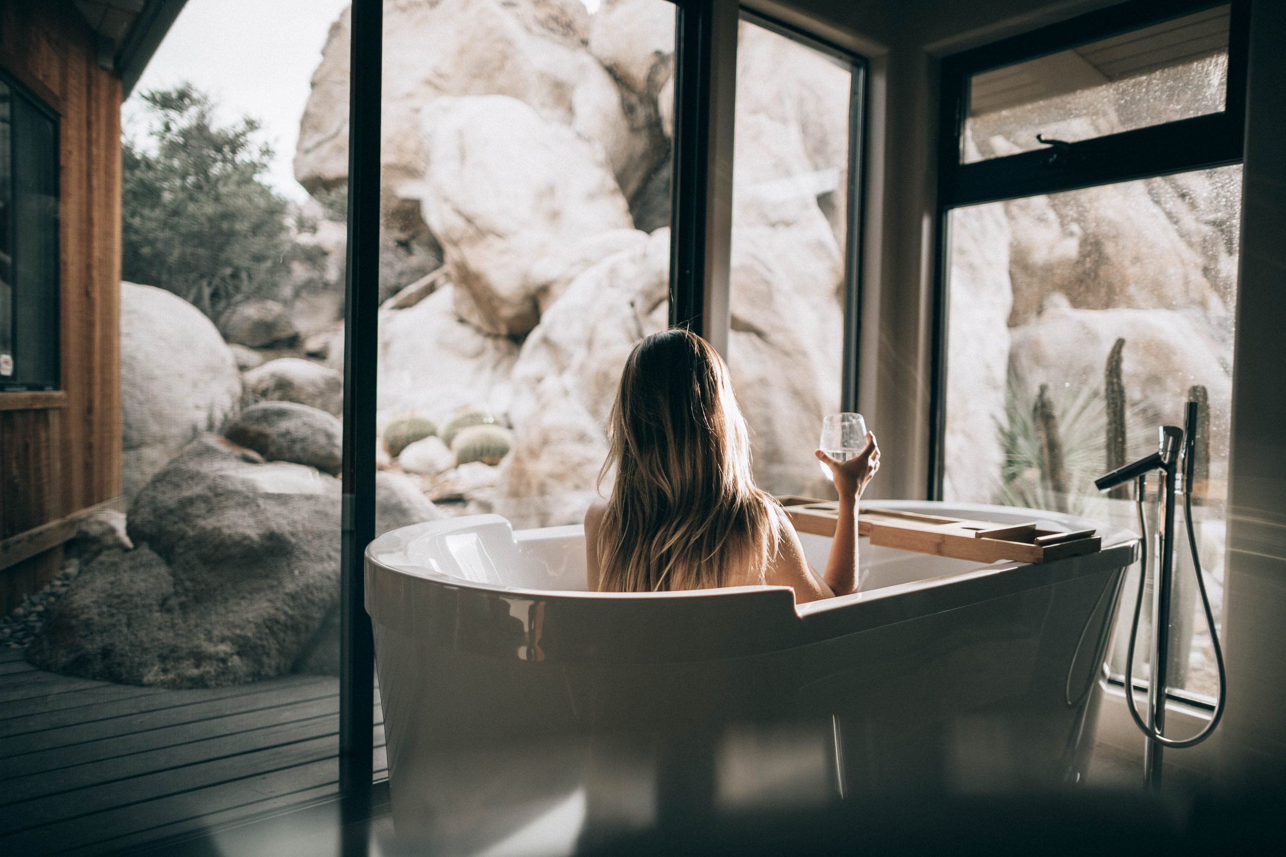 woman sitting in a tub looking out a window at landscaping
