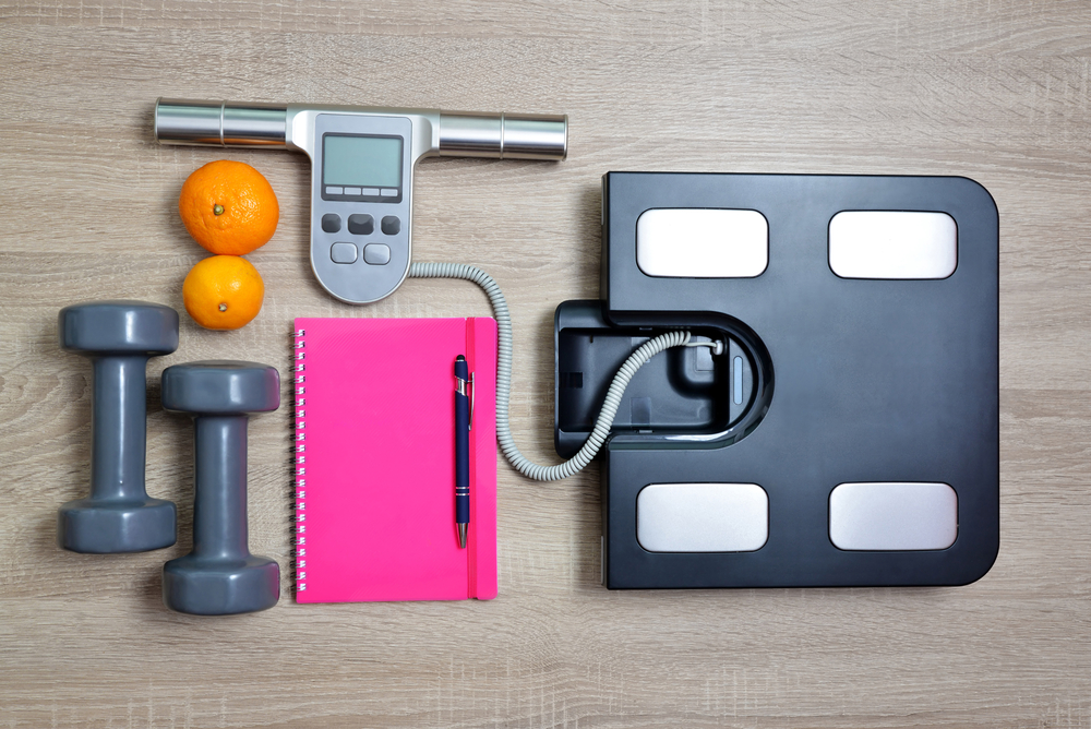 BMI Scale with notebook, free hand weights and two oranges on the ground.