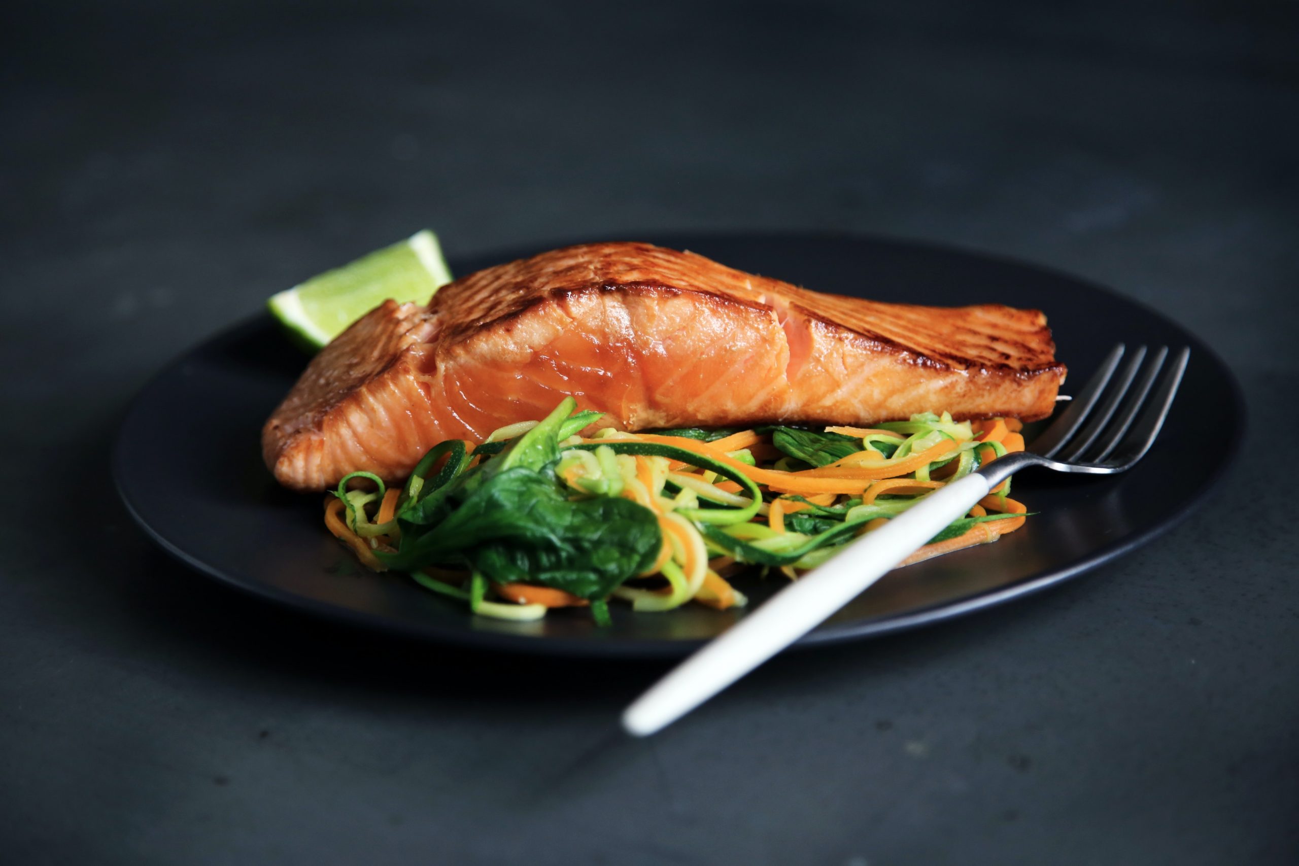 Baked salmon on top of vegetables noodles on a black plate