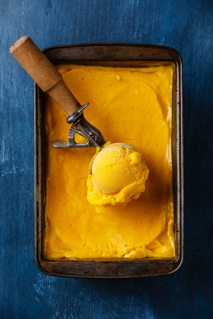Vegan mango ice cream ball in scoop on blue background