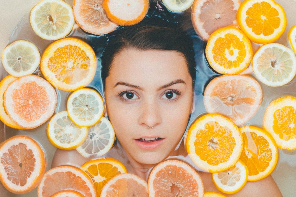 woman in bathtub with slices of oranges, grapefruit and lemons floating in the water. 