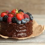 Tasty paleo chocolate cake with different berries on wooden table