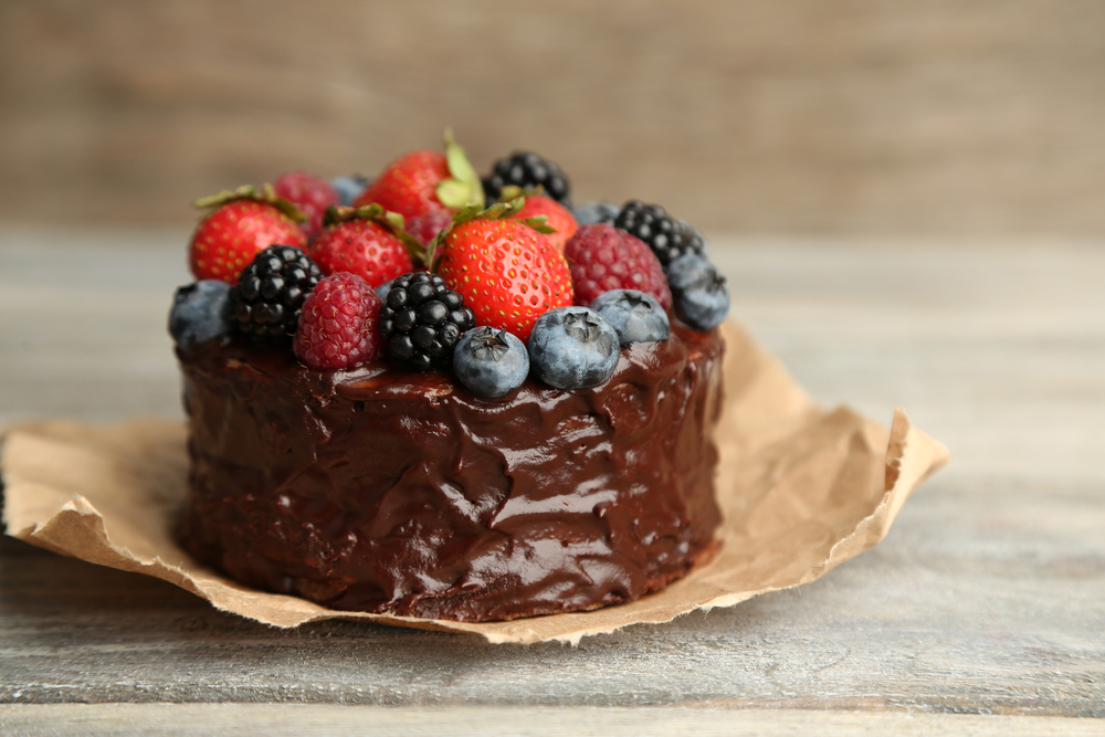 Tasty paleo chocolate cake with different berries on wooden table