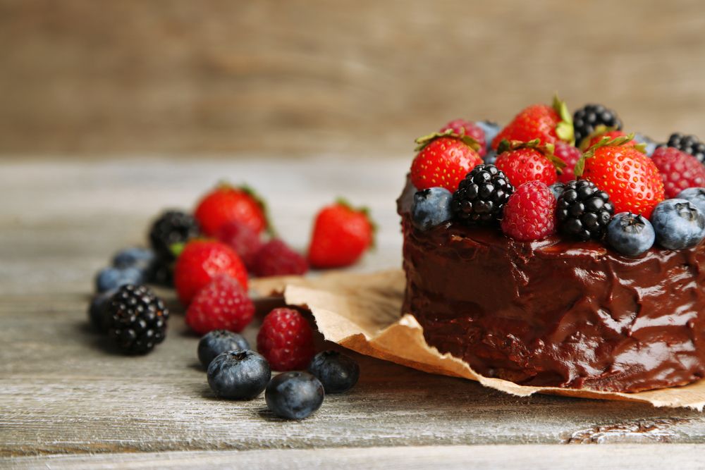 Tasty paleo chocolate cake with different berries on wooden table