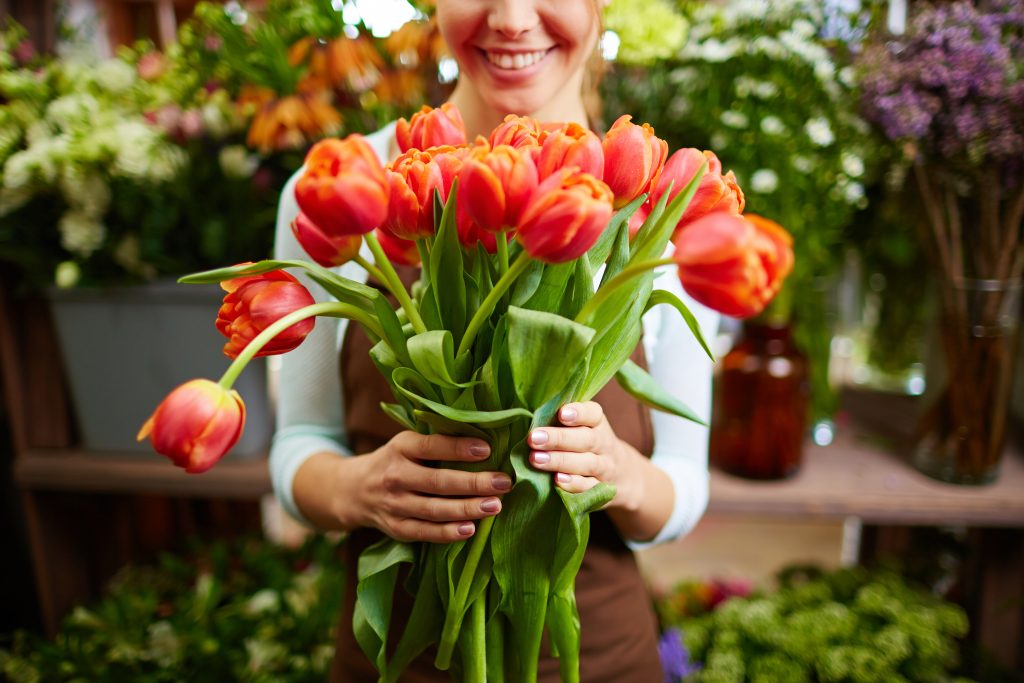 Portrait of happy female florist with bunch of red tulips looking at camera