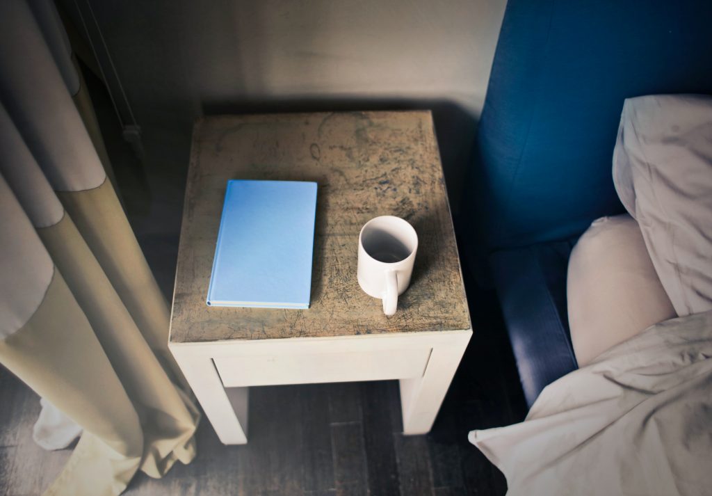 empty mug and notebook on a night stand near a bed