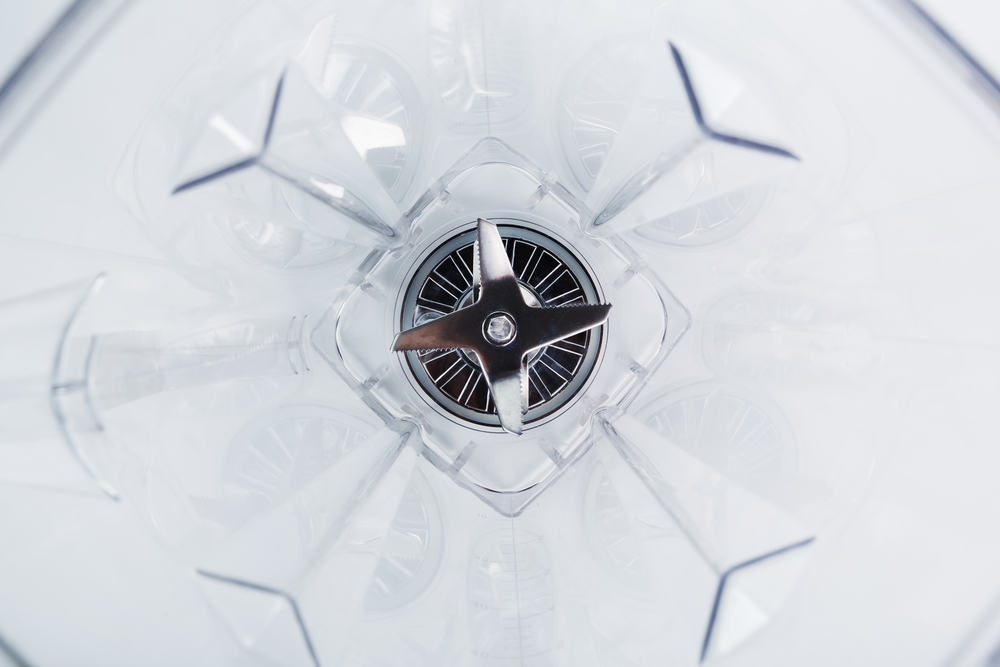 Close-up of a blender glass shot from the inside with sharp stainless steel blades in the center. Inside view, full screen. Conceptual perspective