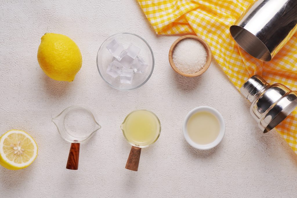 Ingredients to make a lemon drop shot on a counter top - lemons, ice cubes, vodka, lemon wedged, sugar