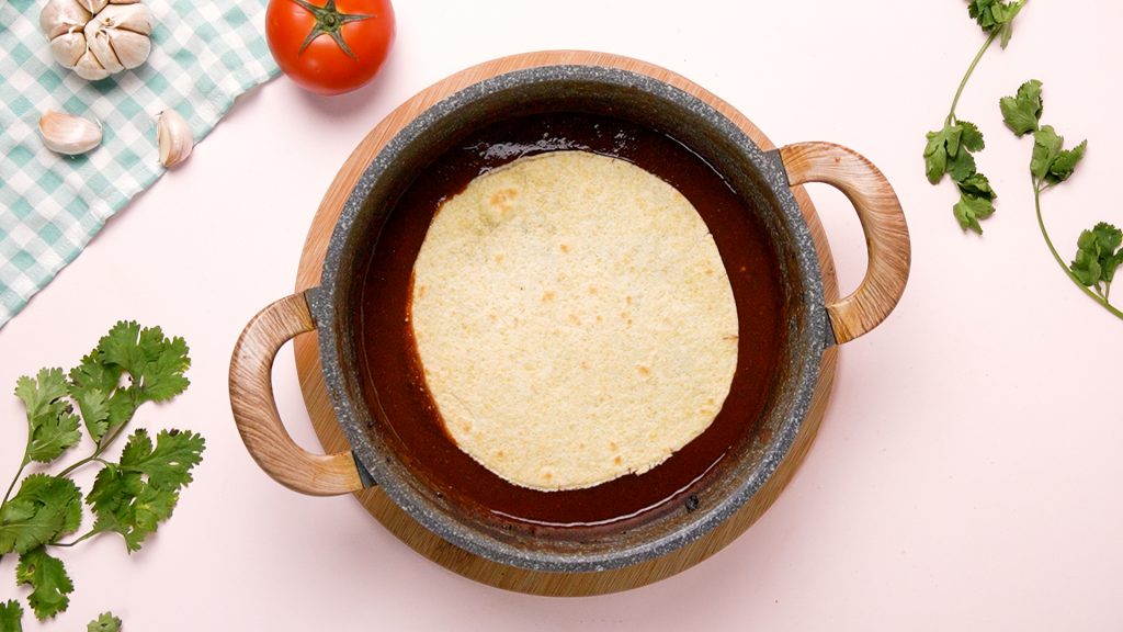 Corn tortilla in sauce in a pan. 