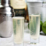 close up of green tea shot with limes and ice in the background