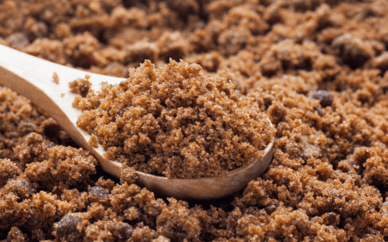 A pile of brown sugar fills the frame, with a wooden spoon heaped with more brown sugar resting on top.
