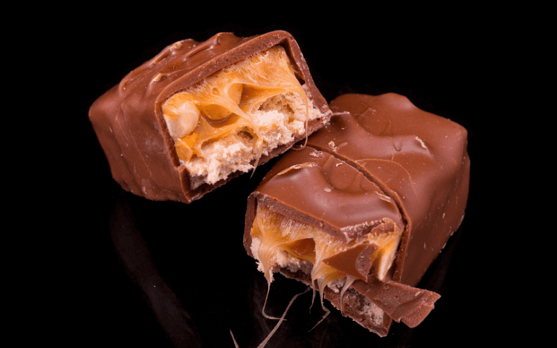 Close-up image: Paleo Snickers bars presented on a sleek black surface.