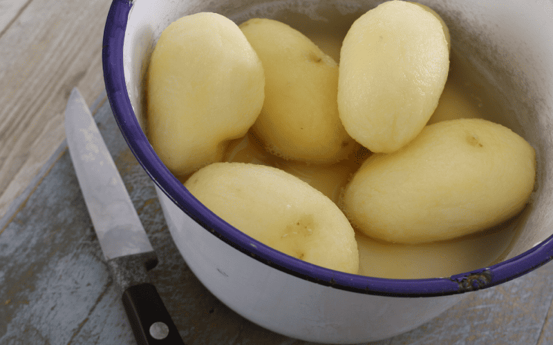 Boiled, whole, and peeled potatoes in a white pan.