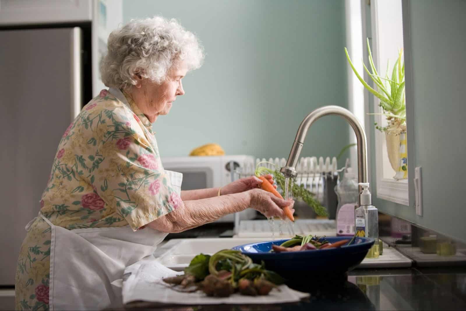 older woman washing vegetables in the sink