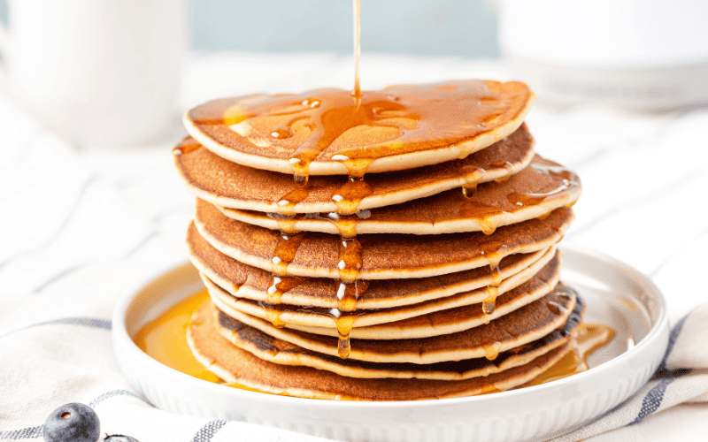 Pancakes stacked on a white plate, generously drizzled with maple syrup