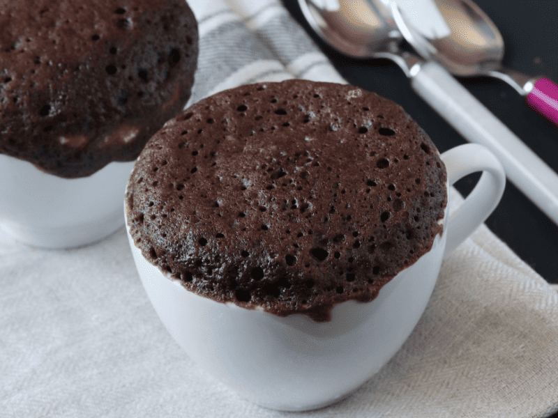 Chocolate protein mug cake on a counter with spoons in the back ground