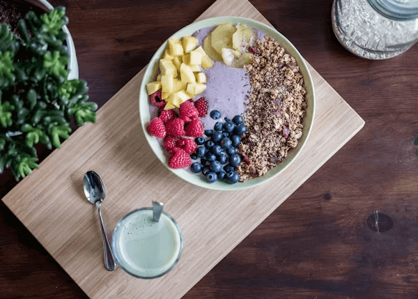 A bowl of cereal with fruit and yogurt on a cutting board