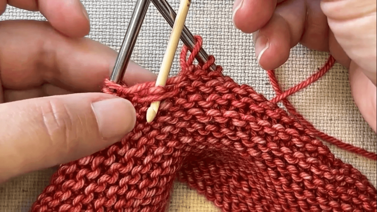 Hands knitting red yarn with needles.