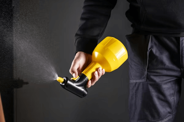 Person using yellow sprayer against black backdrop