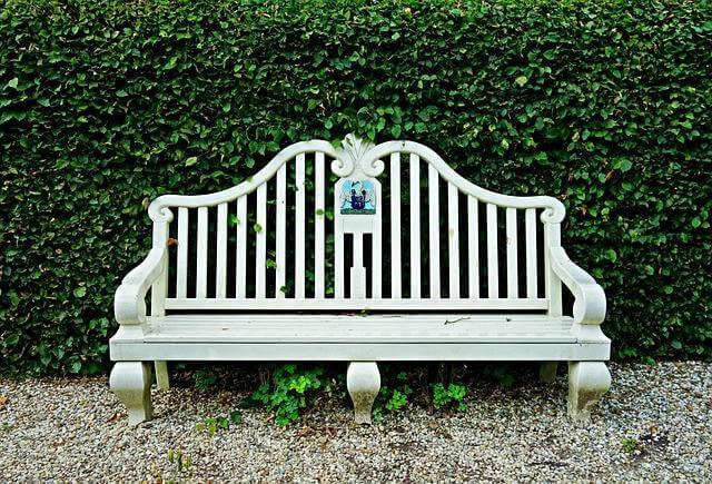 White outdoor bench in front of a green