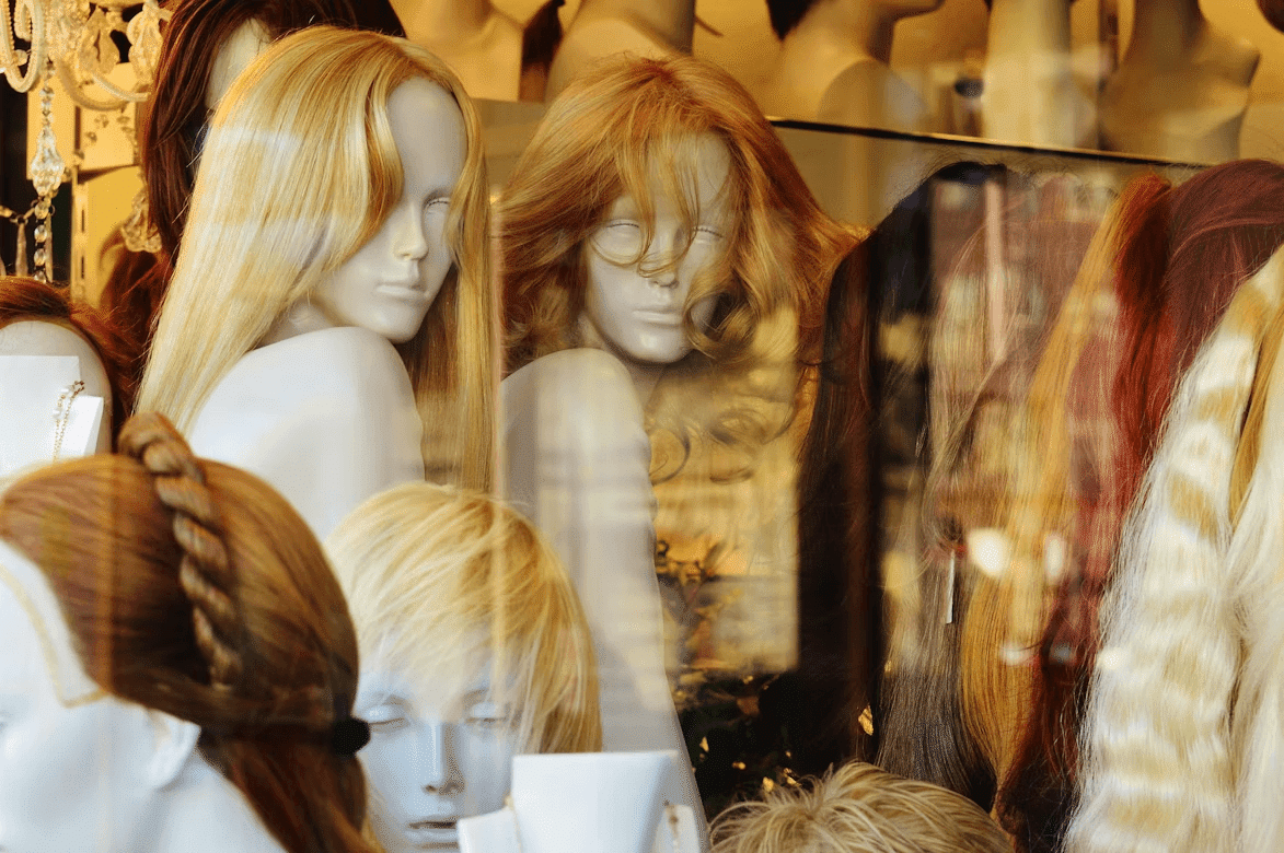The Busy Woman’s Guide to Wigs: How to Get Perfect Hair in Under 5 Minutes Kelly Bejelly Mannequins displaying wigs in a store window.