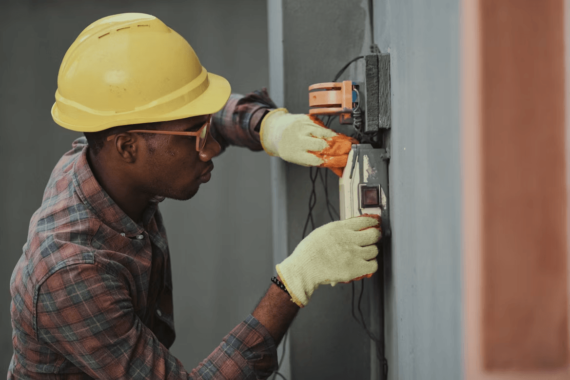 Man in hard hat and gloves repairing an air conditioner