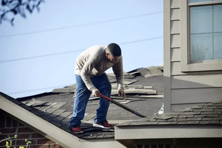 Man inspecting roof for damage with a hammer