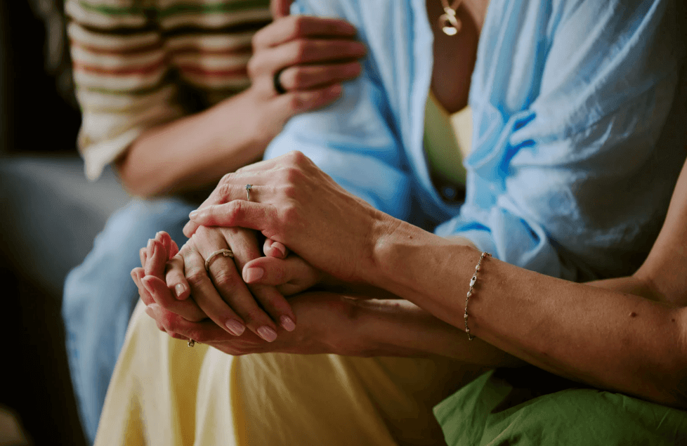 Two women hold hands, symbolizing support in a