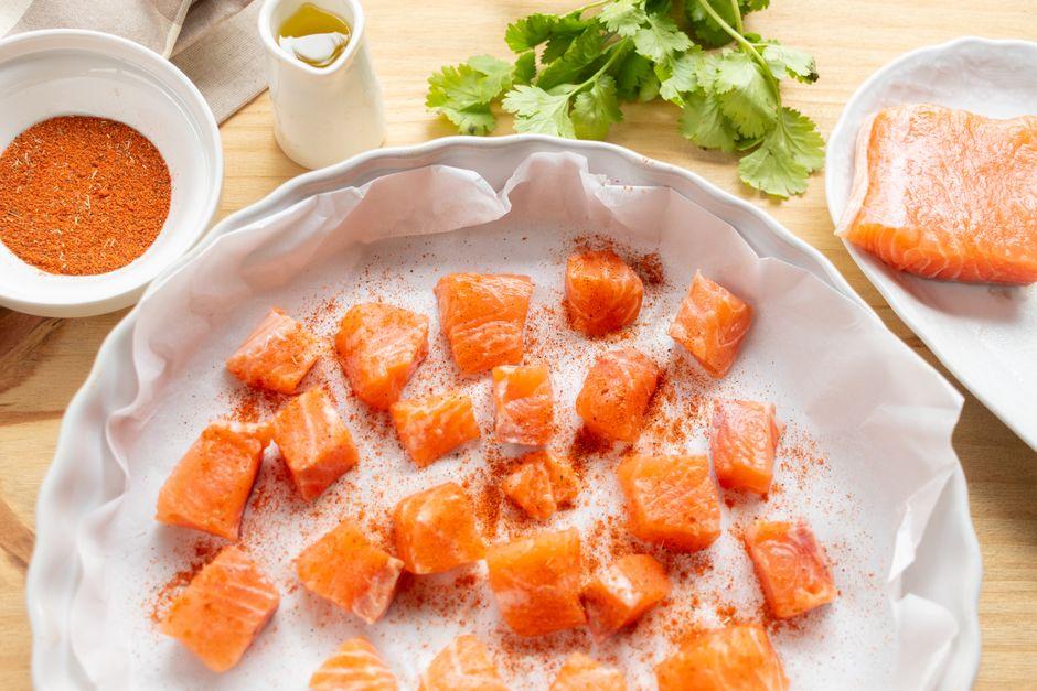 A bowl of salmon, leafy greens and olive oil on a wooden kitchen counter