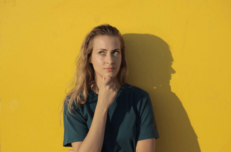 Woman leaning against a yellow wall, hand on chin