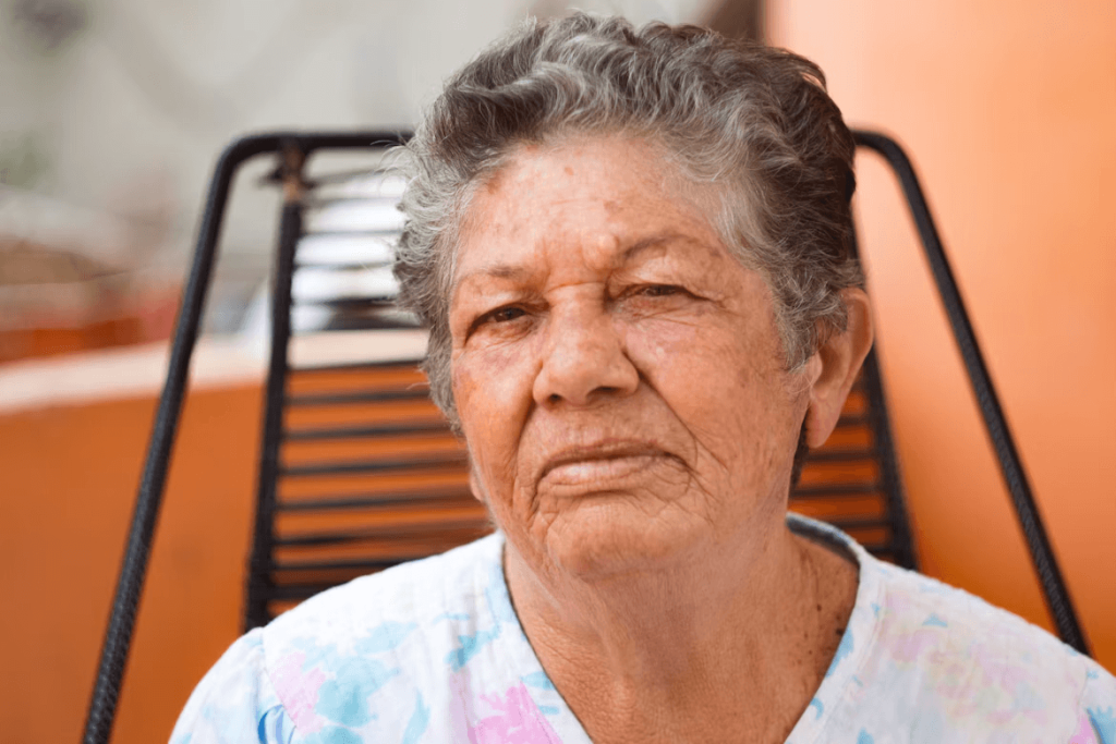 Older woman sitting on a metal chair, looking p