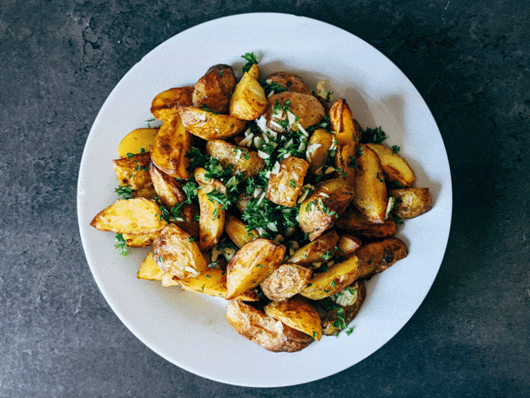 White plate with cooked potatoes and greens