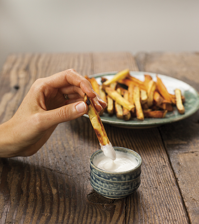 A person holding oven baked fries who is dipping one in the  garlic aip mayo