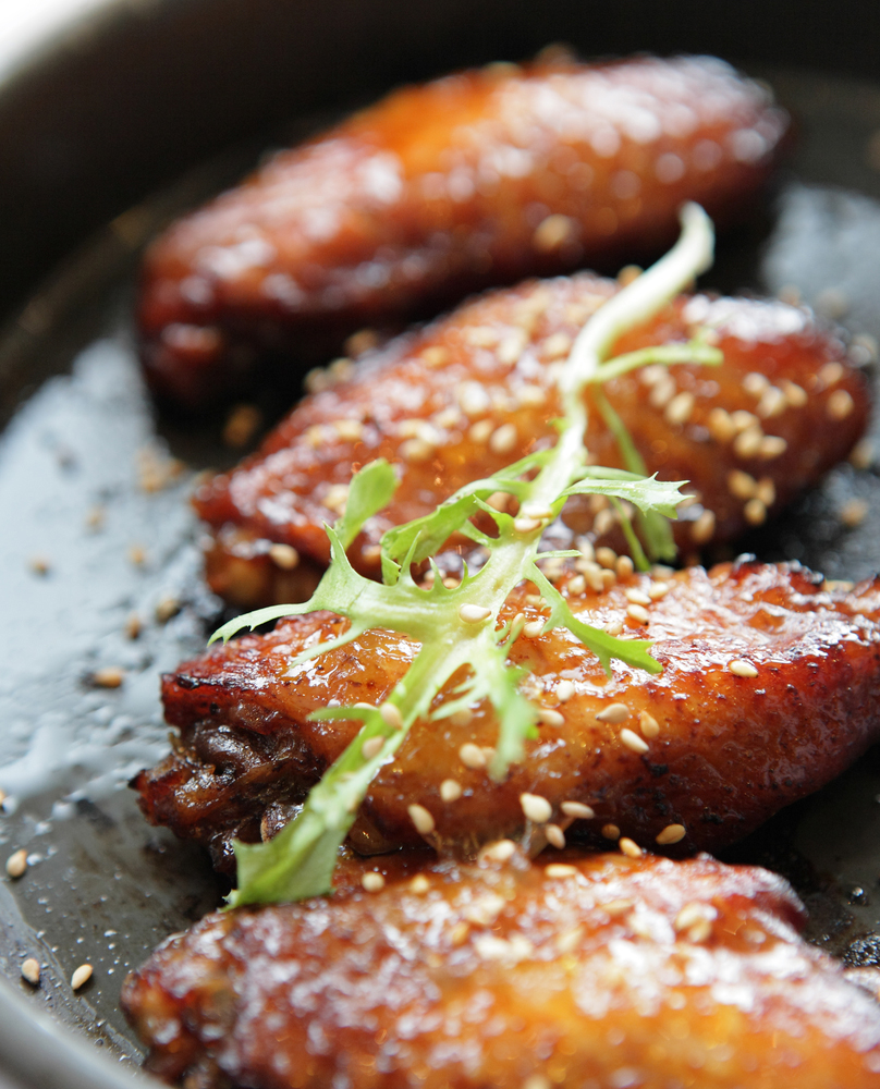 close up of sesame chicken wings in a cast iron skillet with greens on top
